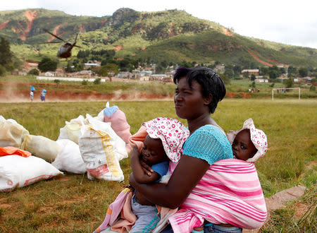 A woman carrying children looks away as a helicopter throws up dust as it takes off after delivering food aid at Ngangu in Chimanimani, Zimbabwe, March 22, 2019. REUTERS/Philimon Bulawayo