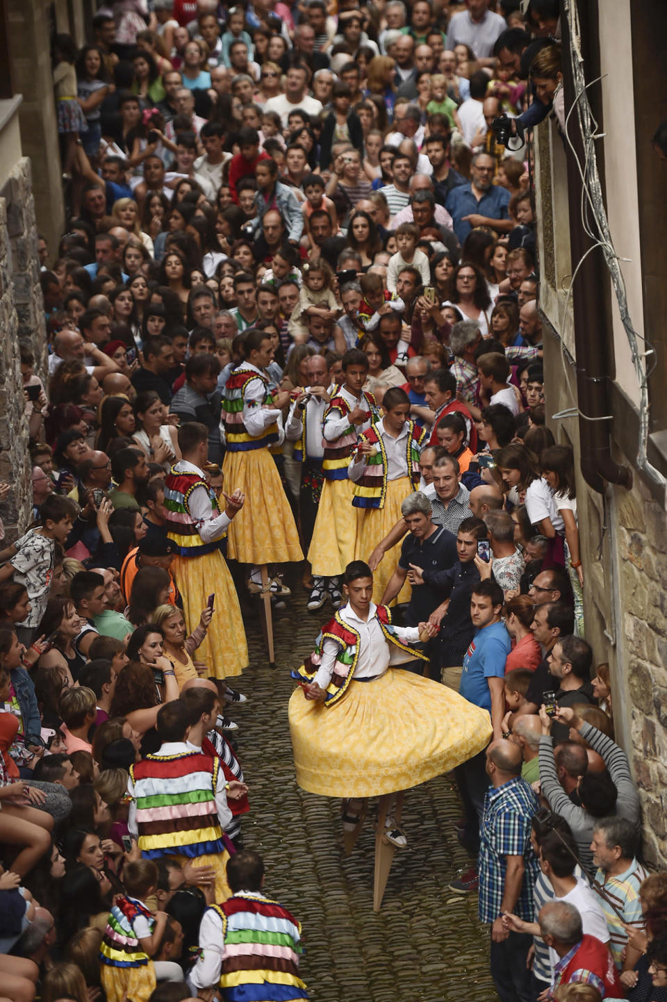 <p>People surround dancers as they perform on stilts in honor of Saint Mary Magdalene in a street for the traditional “Danza de Los Zancos” (Los Zancos Dance), in the small town of Anguiano, northern Spain, Saturday, July 23, 2016. As an ancient tradition for more than 4th centuries, eight young people from the town balance on stilts down the old street, turning to the sound of folk music played on a pipe and drum. (AP Photo/Alvaro Barrientos)</p>