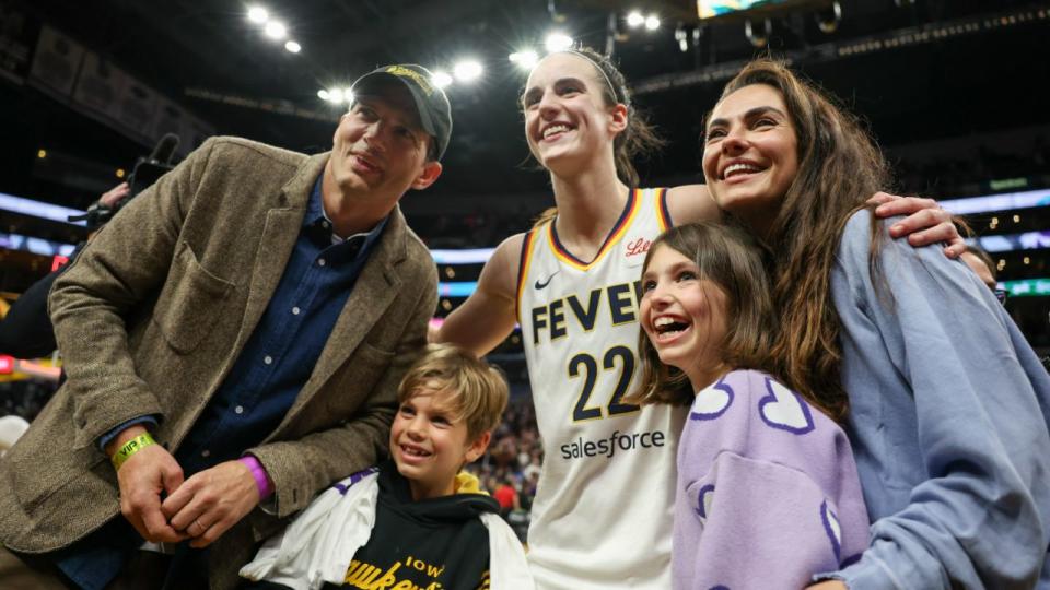 Caitlin Clark #22 of the Indiana Fever poses for a photo with Ashton Kutcher and Mila Kunis, and their kids. Photo by Harry How/Getty Images.