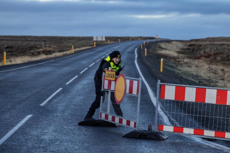 A police officer pulls a barrier to block the road leading to the fishing town of Grindavik, (REUTERS)