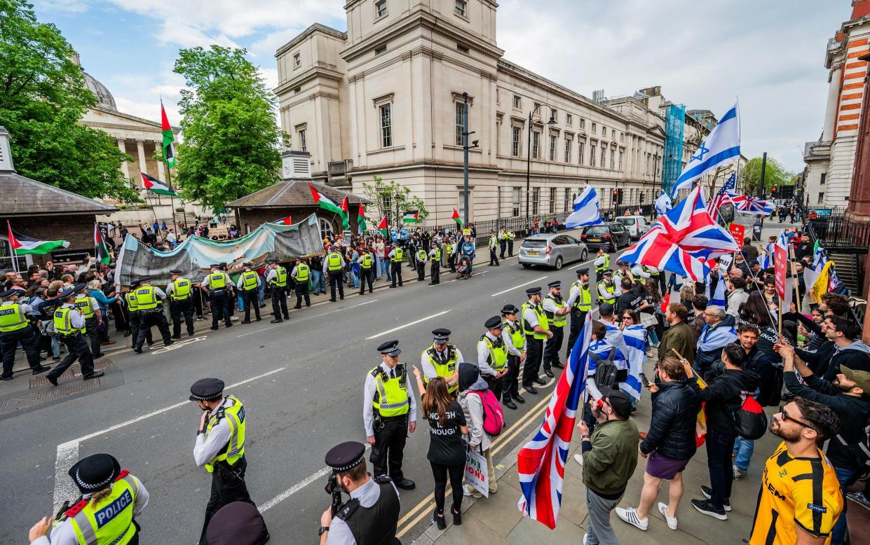 Rival protesters on opposite sides of a London street. One group has British union flags and Israel flags; the other the flag of Palestine. Lines of police separate them