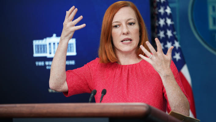 Jen Psaki at the White House briefing podium, raising both hands as she speaks.