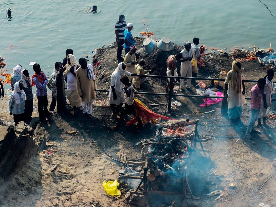 A young boy recycles clothes used to wrap dead bodies for the final rites as onlookers see a funeral pyre burning at Manikarnika Ghat cremation ground in Varanasi.