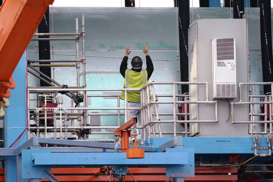 A worker motions as he stands on a platform next to a Boeing 787 fatigue test airframe inside a structural test rig at a massive Boeing airplane production plant Thursday, Oct. 1, 2020, in Everett, Wash. Boeing said Thursday that it will consolidate production of its two-aisle 787 jetliner in South Carolina and shut down the original assembly line for the plane near Seattle. The company said the move will start in mid-2021. (AP Photo/Elaine Thompson)