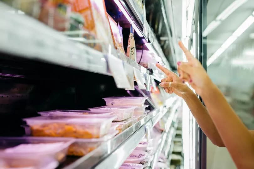 Black single mother and her daughter, selecting take away food from a fridge shelf while shopping in a supermarket