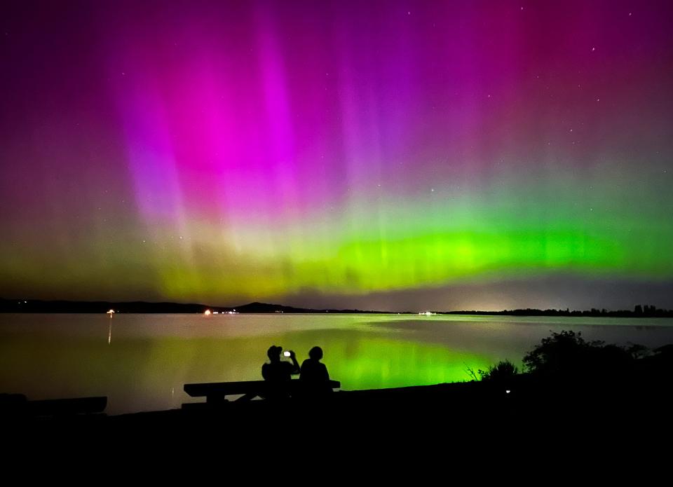 Marshall Falcon, left, photographs the northern lights as he and Angie Avitia watch the celestial display from Perkins Peninsula Park on the shores of Fern Ridge reservoir west of Eugene, Ore. Friday, May 10, 2024.