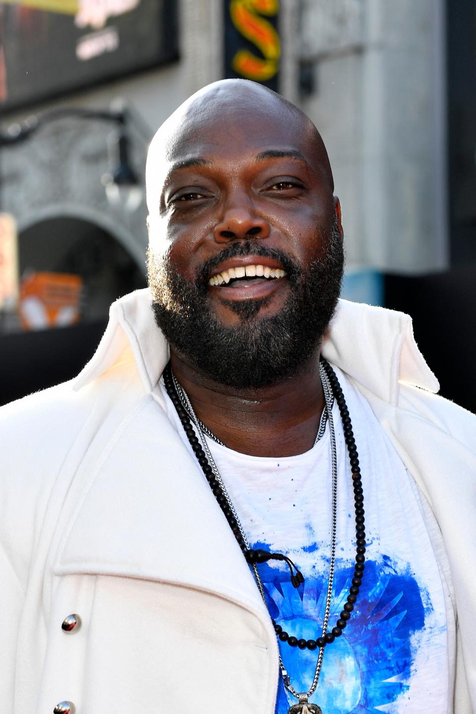 Peter Macon smiling in a white coat with blue graphic tee at the premiere of Kingdom of the Planet of the Apes