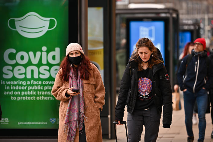 People walk past a green-and-white COVID advisory sign in Edinburgh, Scotland. 