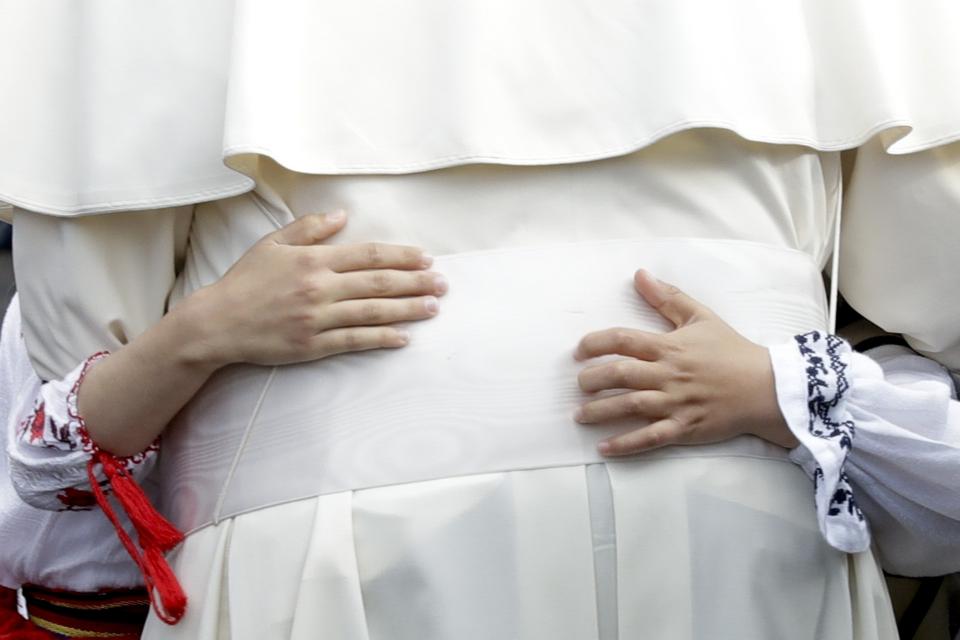 Pope Francis is hugged by a young girl wearing a traditional dress during a meeting with young people and families, in Iasi, Romania, Saturday, June 1, 2019. Francis began a three-day pilgrimage to Romania on Friday that in many ways is completing the 1999 trip by St. John Paul II that marked the first-ever papal visit to a majority Orthodox country. (AP Photo/Andrew Medichini)