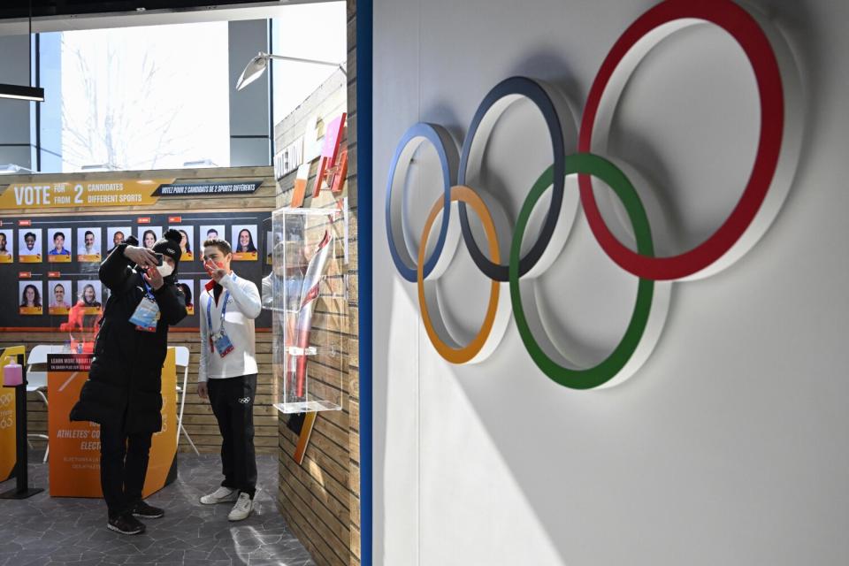 People hold up their phones near a wall displaying the Olympic rings.