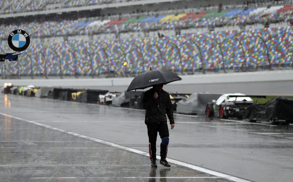 A crew member walks down pit road past the cars sitting idle after the IMSA 24-hour race was red-flagged because of rain at Daytona International Speedway, Sunday, Jan. 27, 2019, in Daytona Beach, Fla. (AP Photo/John Raoux)