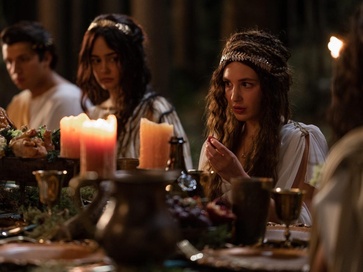 Teen Misty, Travis, Lottie, and Shauna sit at a table decorated with candles and loaded with plates of food while dressed in Roman garb.