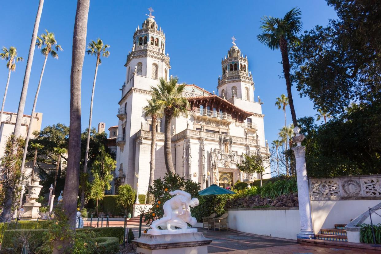 hearst castle from the front showing full facade, towers, palm trees, sun, clear blue sky