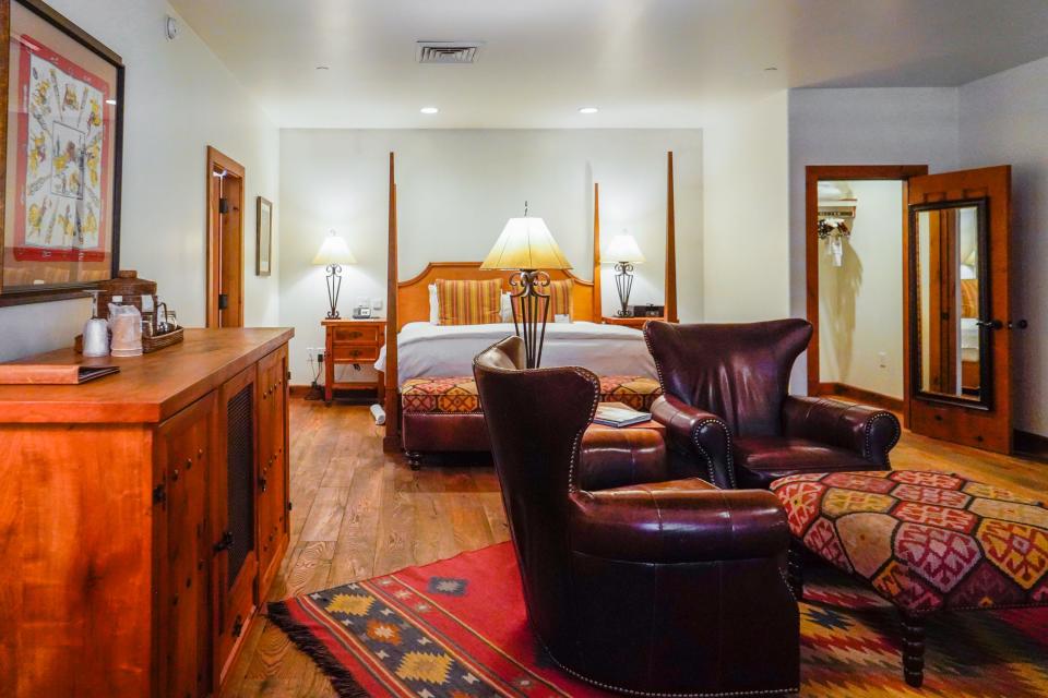 Inside a western-style room with brown leather chairs, a king size bed, and a red rug