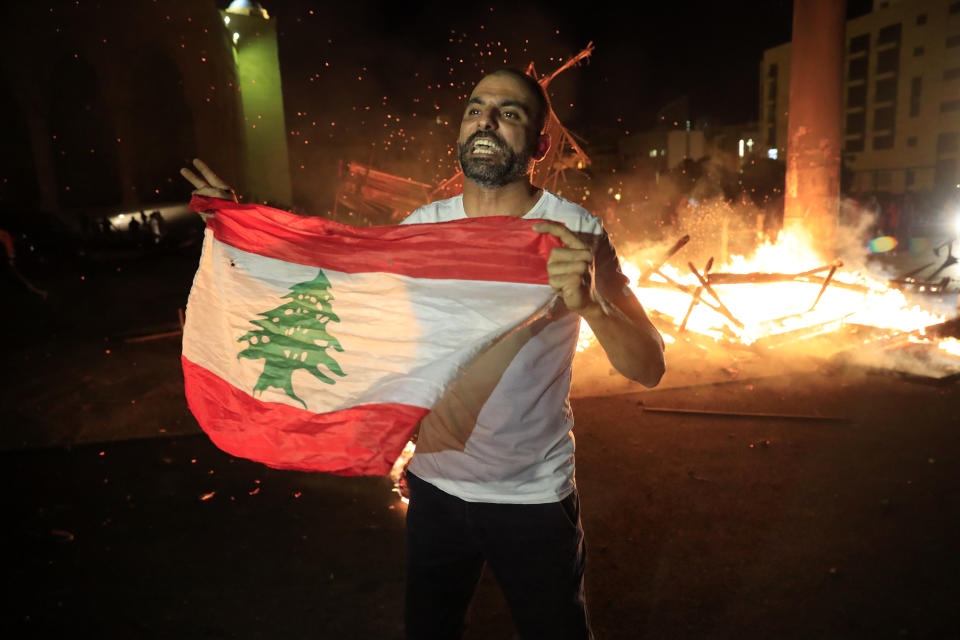 A protester holds the Lebanese flag and shouts slogans denouncing the naming of former Lebanese Prime Minister Saad Hariri as a potential candidate for prime minister, after Hariri's supporters burned a significant protest symbol erected in downtown Beirut, Lebanon, Wednesday, Oct. 21, 2020. Hariri resigned a year ago amid nationwide protests against government corruption and mismanagement of Lebanon's resources. (AP Photo/Hussein Malla)