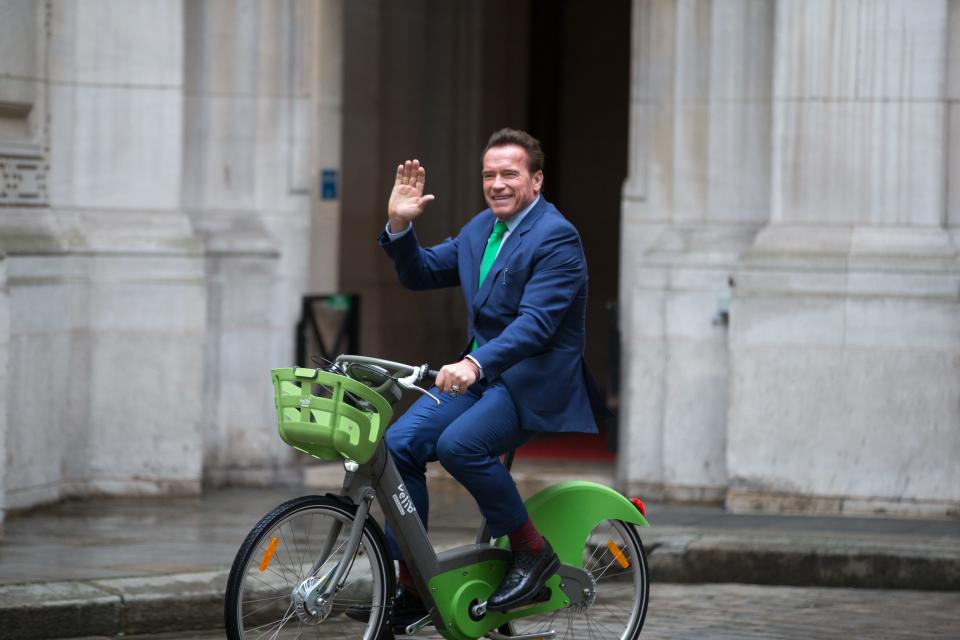 Former Governor of the US State of California Arnold Schwarzenegger (C) waves as he rides a bicycle in Paris on December 11, 2017, on the sidelines of meetings with Mayor of Paris Anne Hidalgo.  (Photo by Michel Stoupak/NurPhoto via Getty Images)