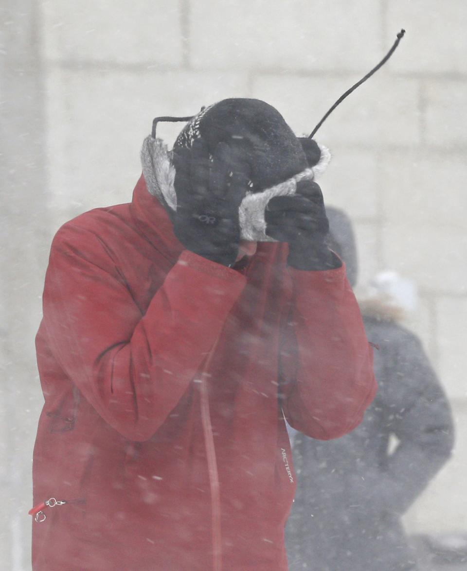 A man covers his face as he walks in the street during a snowstorm in Quebec City