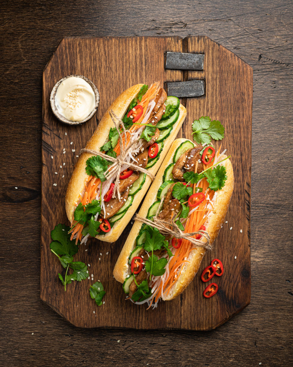 Two sub sandwiches tied with twine on a wood cutting board