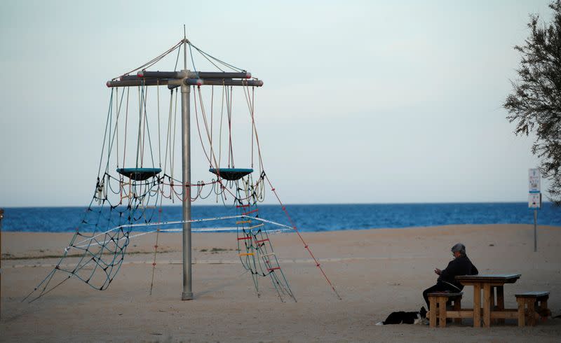 An elderly man sits with a dog in front of a closed playground, following the coronavirus disease (COVID-19) outbreak in El Masnou