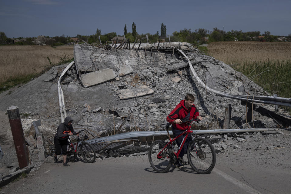 Teenagers on bicycles pass a bridge destroyed by shelling near Orihiv, Ukraine, Thursday, May 5, 2022. (AP Photo/Evgeniy Maloletka)
