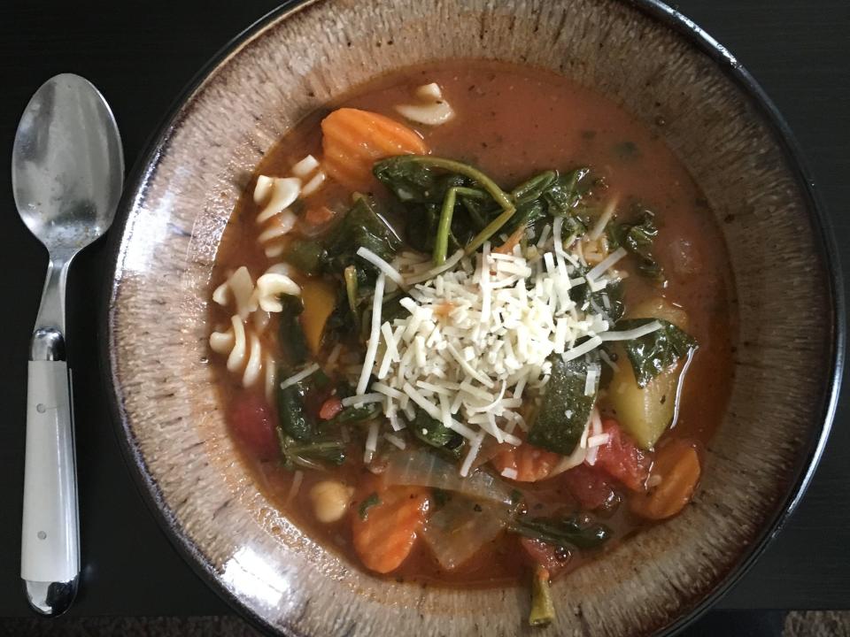 MINESTRONE SOUP with cheese topping in brown bowl with spoon beside it