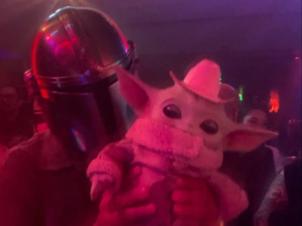 A man in a Mandalorian mask lifts up his baby Grogu doll that’s wearing a tiny sombrero atop his head. (Olivia Hebert)