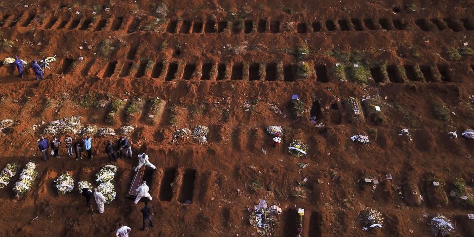 Gravediggers wearing protective suits bury the coffin of a person who died from the coronavirus disease (COVID-19), as open graves are seen at Vila Formosa cemetery, Brazil's biggest cemetery, in Sao Paulo, Brazil, May 22, 2020. Picture taken with a drone. REUTERS/Amanda Perobelli