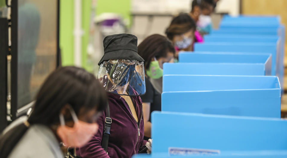 C.K. Hoffler, center, wears a face shield as she voted at Cross Keys High School in Atlanta on Tuesday, June 9, 2020. At the DeKalb County school, volunteers passed out water bottles to a crowd of 100 voters lined up for hours outside the building. (John Spink/Atlanta Journal-Constitution via AP)