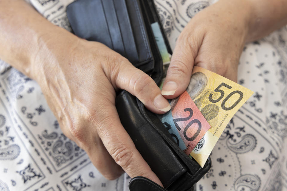 Mature adult (45-49 years) holding a wallet containing some Australian bank notes. 