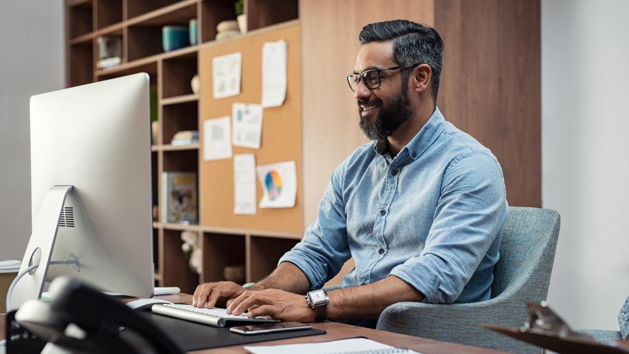 Smiling creative business man typing on desktop computer in office.