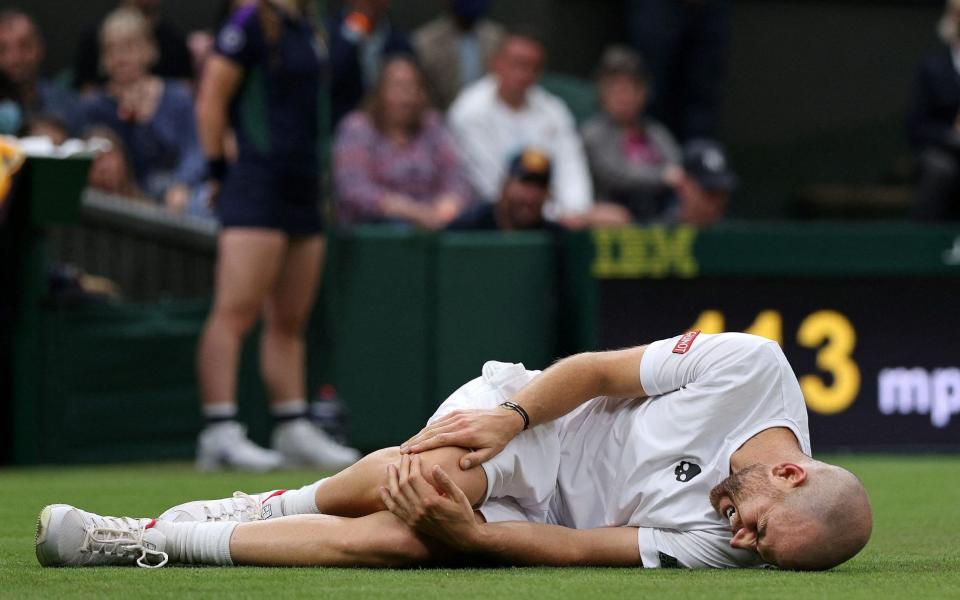 France's Adrian Mannarino holds his knee after slipping on the grass during play against Switzerland's Roger Federer - AFP