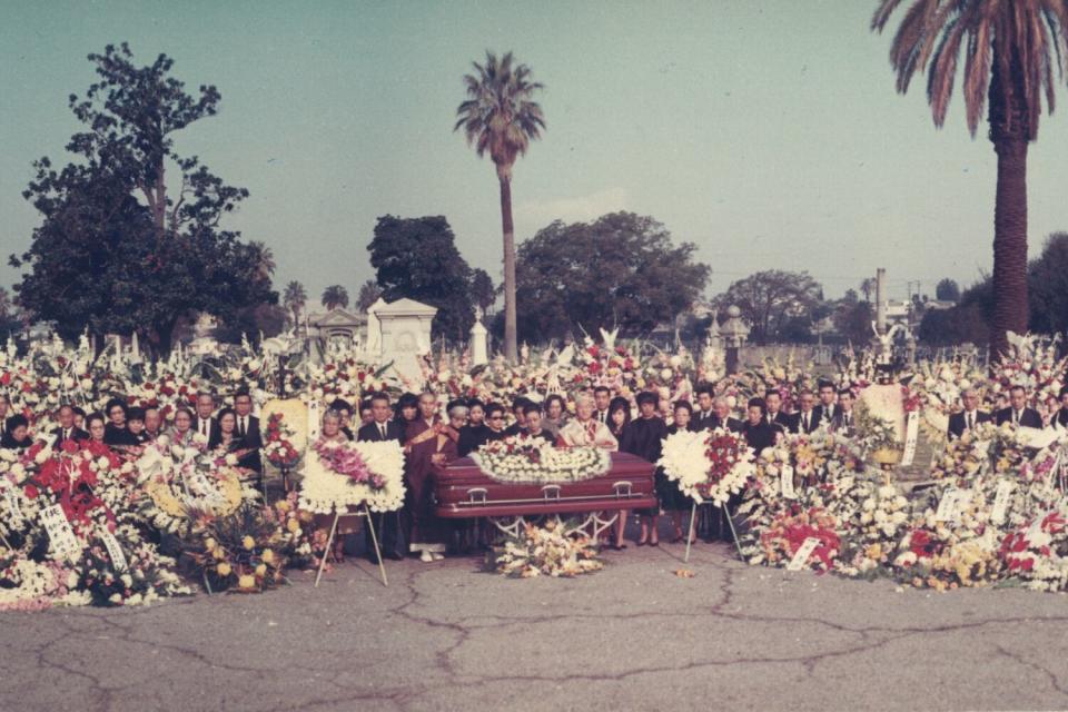 Scores of people gather around a casket.