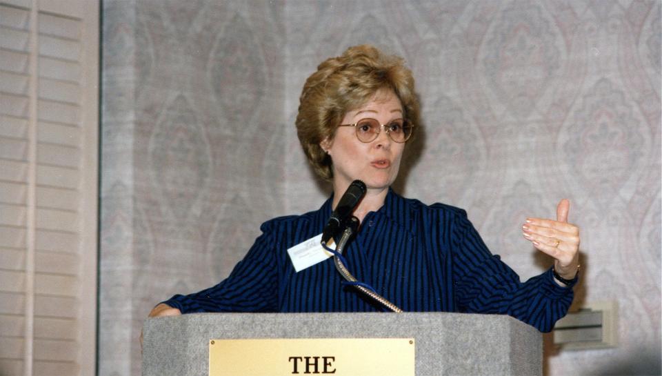 Dorothy Swanson wearing very '80s glasses on a podium at a VQT event.
