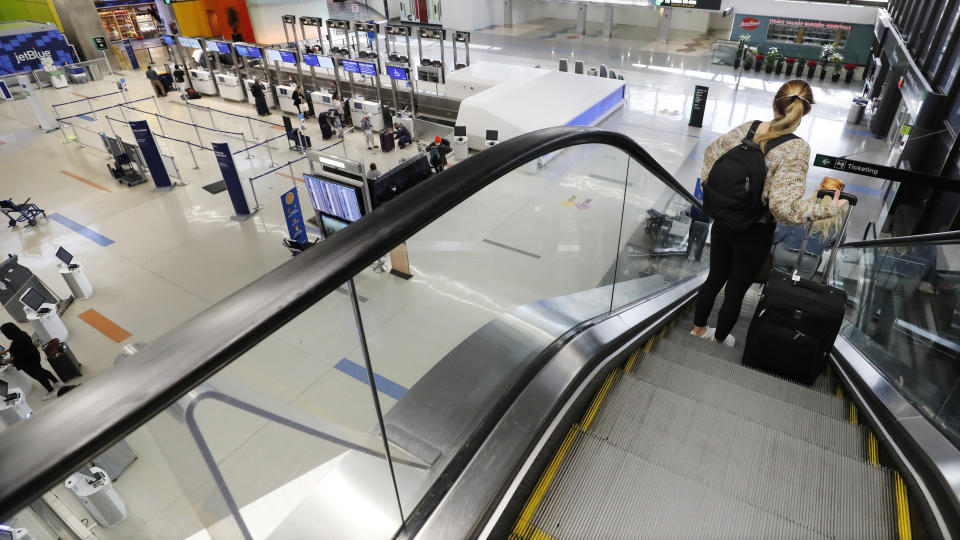 A traveler rides an escalator with her luggage as she arrives at the nearly empty JetBlue terminal at Logan Airport, Friday Nov. 20, 2020, in Boston. With the coronavirus surging out of control, the nation's top public health agency pleaded with Americans not to travel for Thanksgiving and not to spend the holiday with people from outside their household. (AP Photo/Michael Dwyer)