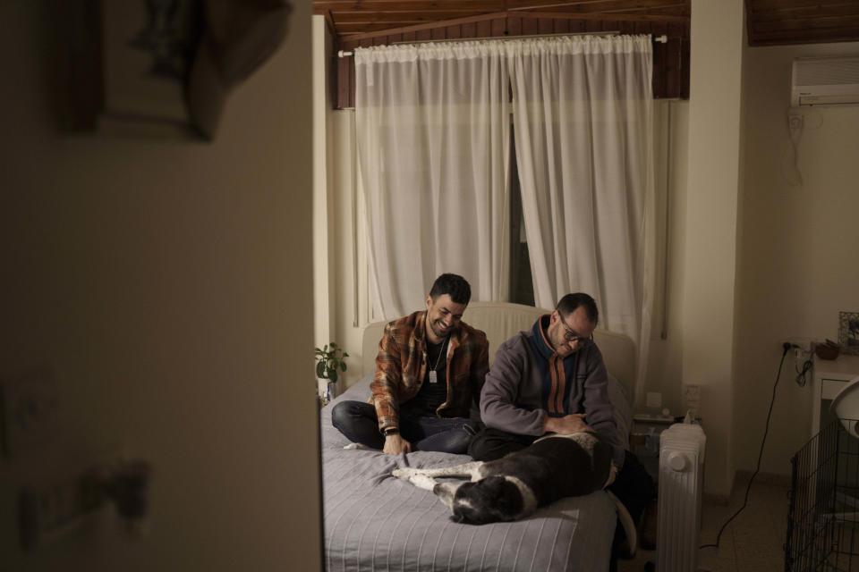 Residents of Kibbutz Nahal Oz, Nadav Tzabari left, Rotem Katz sit on the bed with their dog in a small apartment in Kibbutz Mishmar HaEmek, northern Israel, Sunday, Feb. 4, 2024. (AP Photo/Leo Correa)