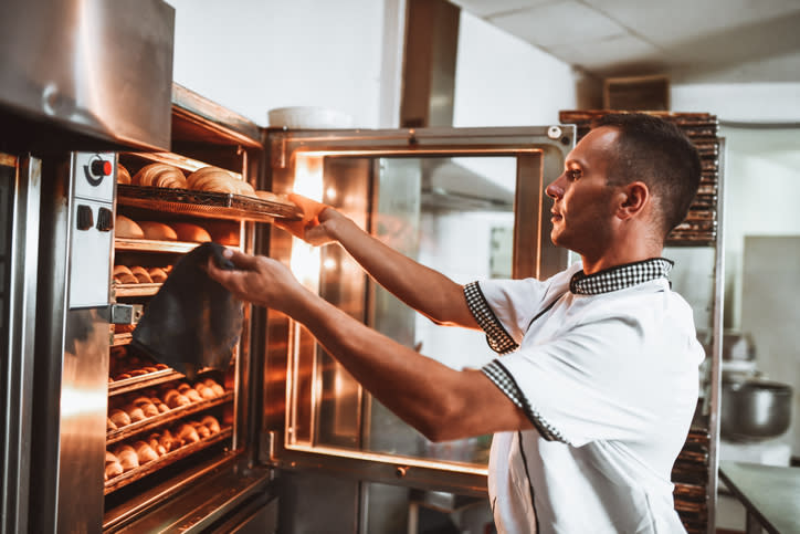 Baker placing trays of bread into an industrial oven