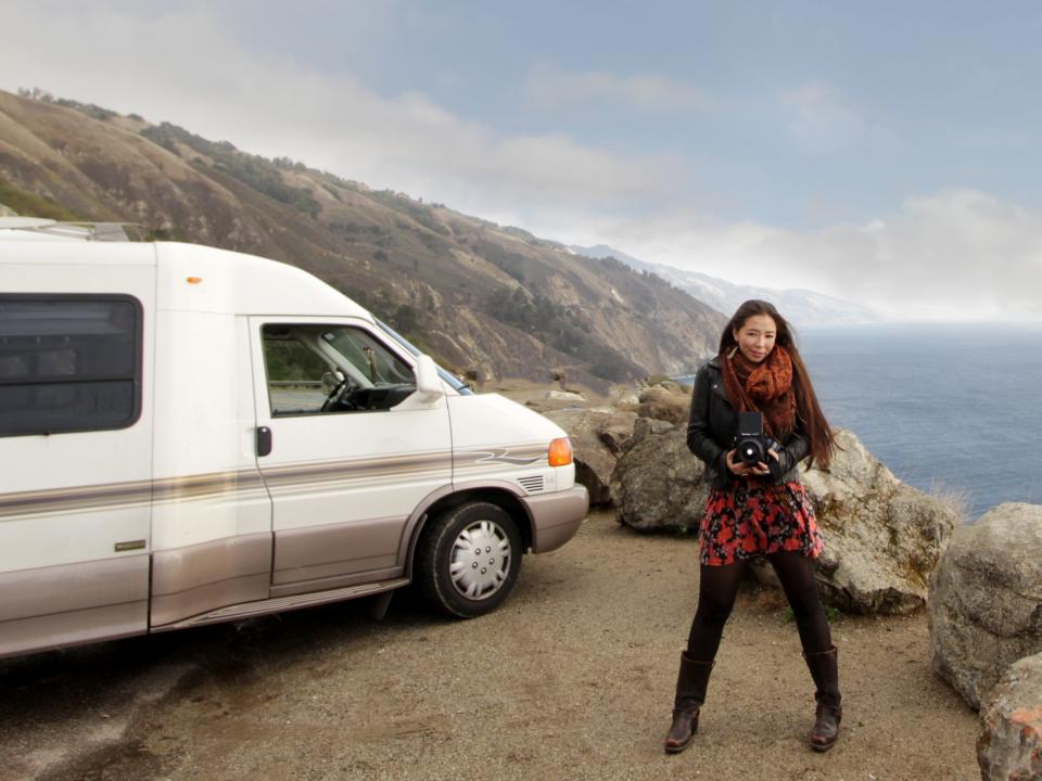 A self portrait of Matika Wilbur. A woman stands next to a van on the edge of a cliff.