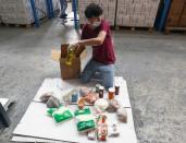 A volunteer wearing a protective mask and gloves fills a box with food for distribution to people in need, in Beirut