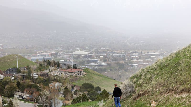 The Wasatch Mountains are barely visible on a windy day as a walker hikes in the foothills of Salt Lake City on Thursday, April 21, 2022.