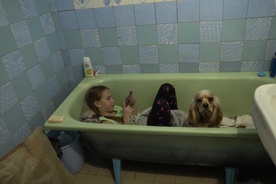 Zlata-Maria Shlapak, sits inside a bathtub with her puppy Letti, as an air siren goes off, at an apartment her family took refuge in and currently renting, in Lviv, western Ukraine, Saturday, April 2, 2022. Zlata didn't see much fighting in Kharkiv, but "when she hears loud noises, she tries to hide," her mother says. (AP Photo/Nariman El-Mofty)