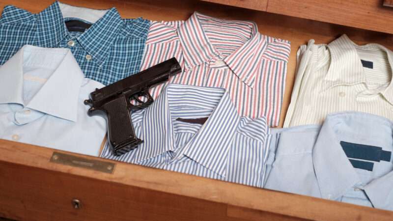 A handgun sits atop a row of folded shirts in a dresser drawer.