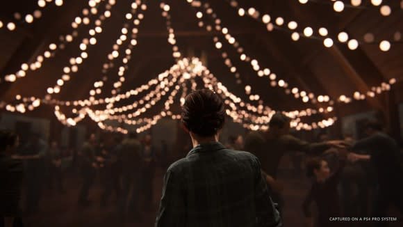 Ellie from Sony's The Last of Us 2 looking at decorative lights inside of a barn.