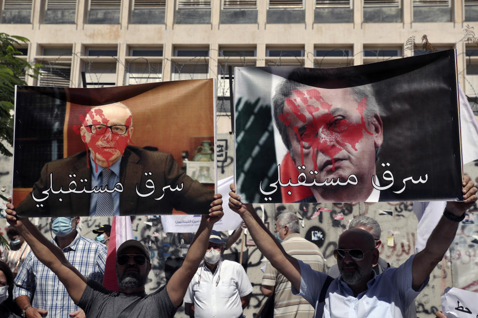 FILE - Bank customers hold up defaced posters of Riad Salameh, the governor of Lebanon's Central Bank, right, and Makram Sadir, then-secretary general of the Association of Banks in Lebanon, with Arabic that reads: "Stole my future," during a protest in front of the Central Bank in Beirut, Lebanon, Wednesday, Oct. 6, 2021. Lebanese caretaker Justice Minister Henry Khoury said on Wednesday, Jan. 11, 2023 a European judicial delegation from France, Germany, and Luxembourg have started to arrive in Lebanon as they continue probing Central Bank Governor Riad Salameh and affiliates over corruption allegations. (AP Photo/Bilal Hussein, File)