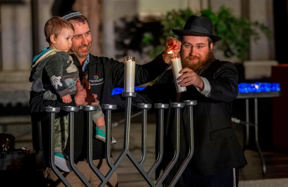 Rabbi Matt Rosenberg, center, holds his son Solomon Rosenberg, 1, while lighting a menorah with Rabbi Moshe Cohen during a Hanukkah celebration by Chabad Greater Sacramento on Thursday at the Capitol.