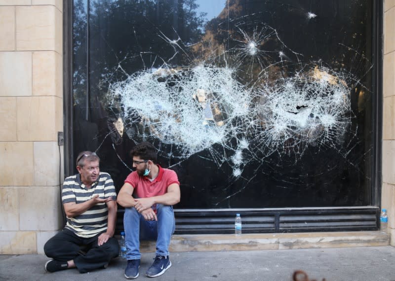 Demonstrators talk as they sit next to a shop with a broken window during a protest targeting the government over an economic crisis, in Beirut