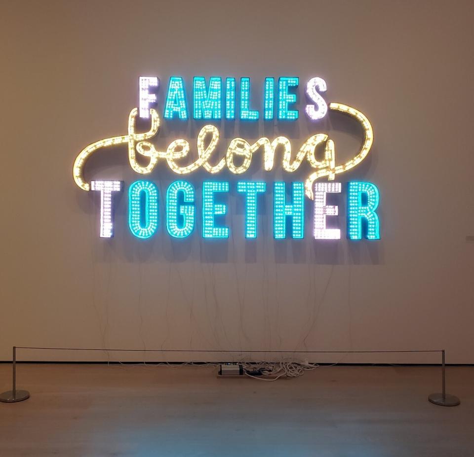 A sign reading 'Families belong together' made of cardboard and LED lights