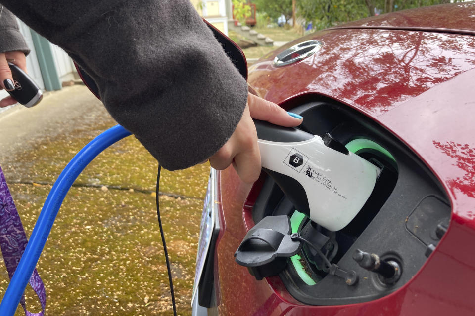 Rebecca DeWhitt charges her electric vehicle in the driveway of the Portland, Ore., home she rents on Sept. 30, 2022. DeWhitt and her partner aren't allowed to use the rental home's garage and so they charge their EV using an extension cord that plugs into a standard electrical outlet outside their front door. The great transition to electric vehicles is underway for homeowners who can charge their cars in a private garage, but for millions of renters like DeWhitt, access to charging remains a significant barrier. (AP Photo/Gillian Flaccus)