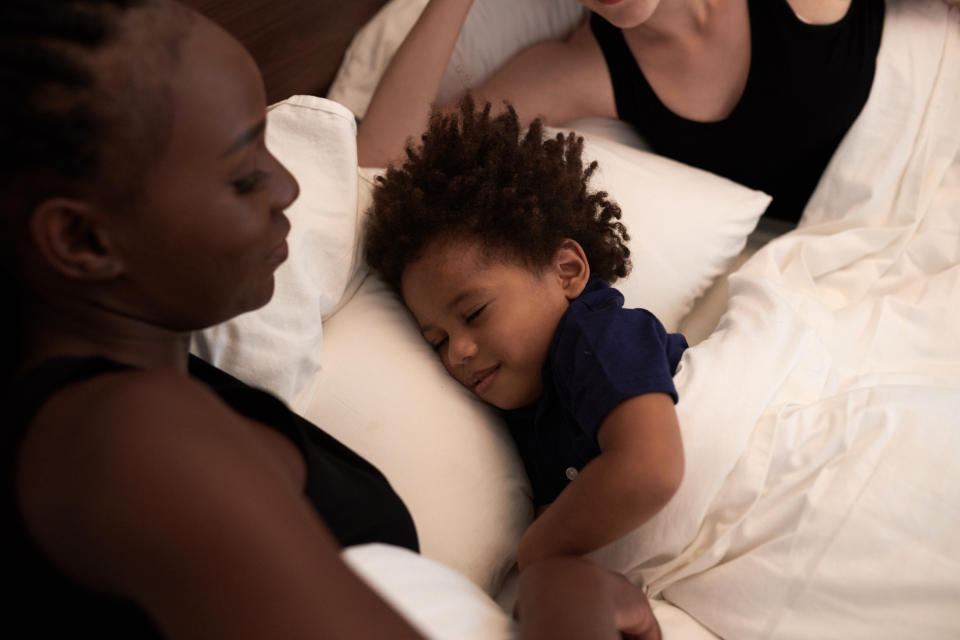 A little boy sleeps with a smile on his face between his two mothers in bed