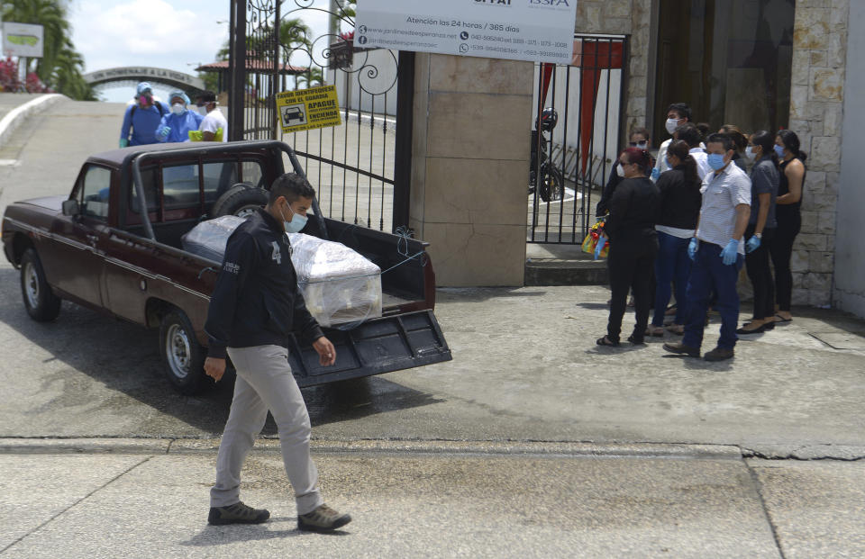 Relatives watch as the remains of a coronavirus victim, which authorities wrap in plastic, arrive to the Jardines de la Esperanza cemetery in Guayaquil, Ecuador, Wednesday, April 1, 2020. Ecuador has one of the highest numbers of confirmed coronavirus cases and deaths in the region, combined with a lack of ventilators, hospital beds and experienced crisis management. (AP Photo/Andrea Aguilar)