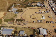 FILE- In this drone file photo taken Saturday May 2, 2020, thousands line up to receive food handouts in the Olievenhoutbos township of Midrand, South Africa. South Africa is struggling to balance its fight against the coronavirus with its dire need to resume economic activity. The country with the Africa’s most developed economy also has its highest number of infections — more than 19,000. (AP Photo/Jerome Delay, File)